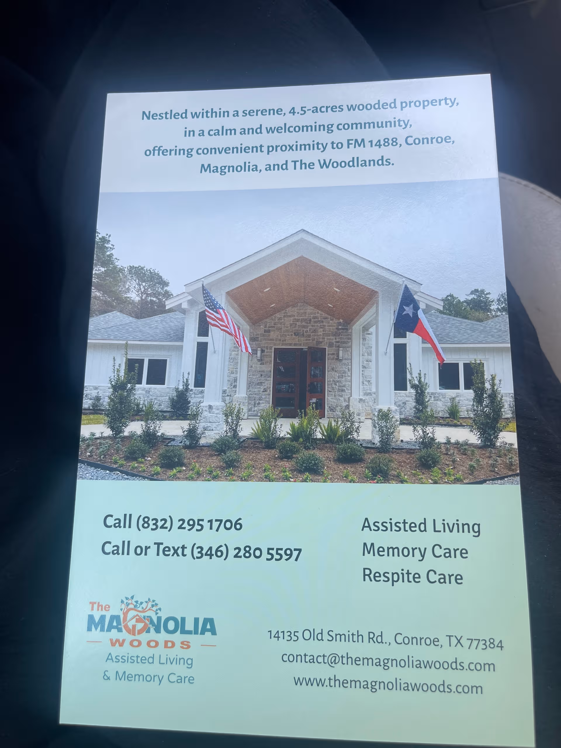 Front view of Magnolia Woods Assisted Living building with entrance, landscaping, and flags.