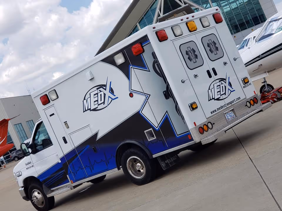 MedEx Medical Transport ambulance parked outside a modern glass-front facility.