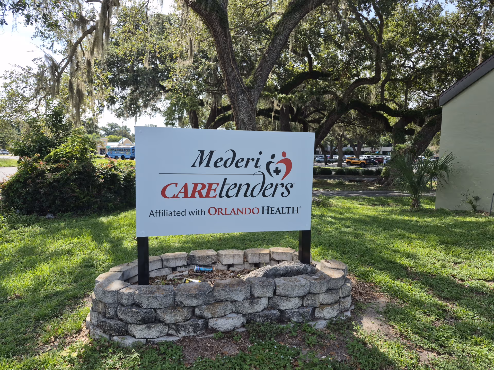 Mederi Caretenders sign in a grassy, tree-filled outdoor area.