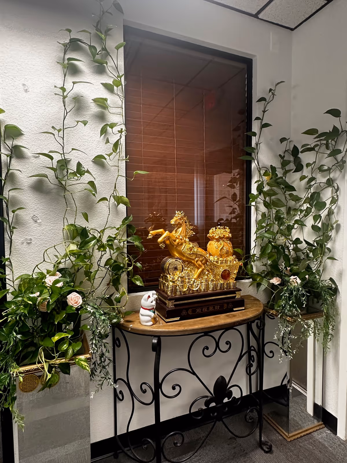 Indoor corner with a wooden table, greenery, and a golden ornamental statue by a window.