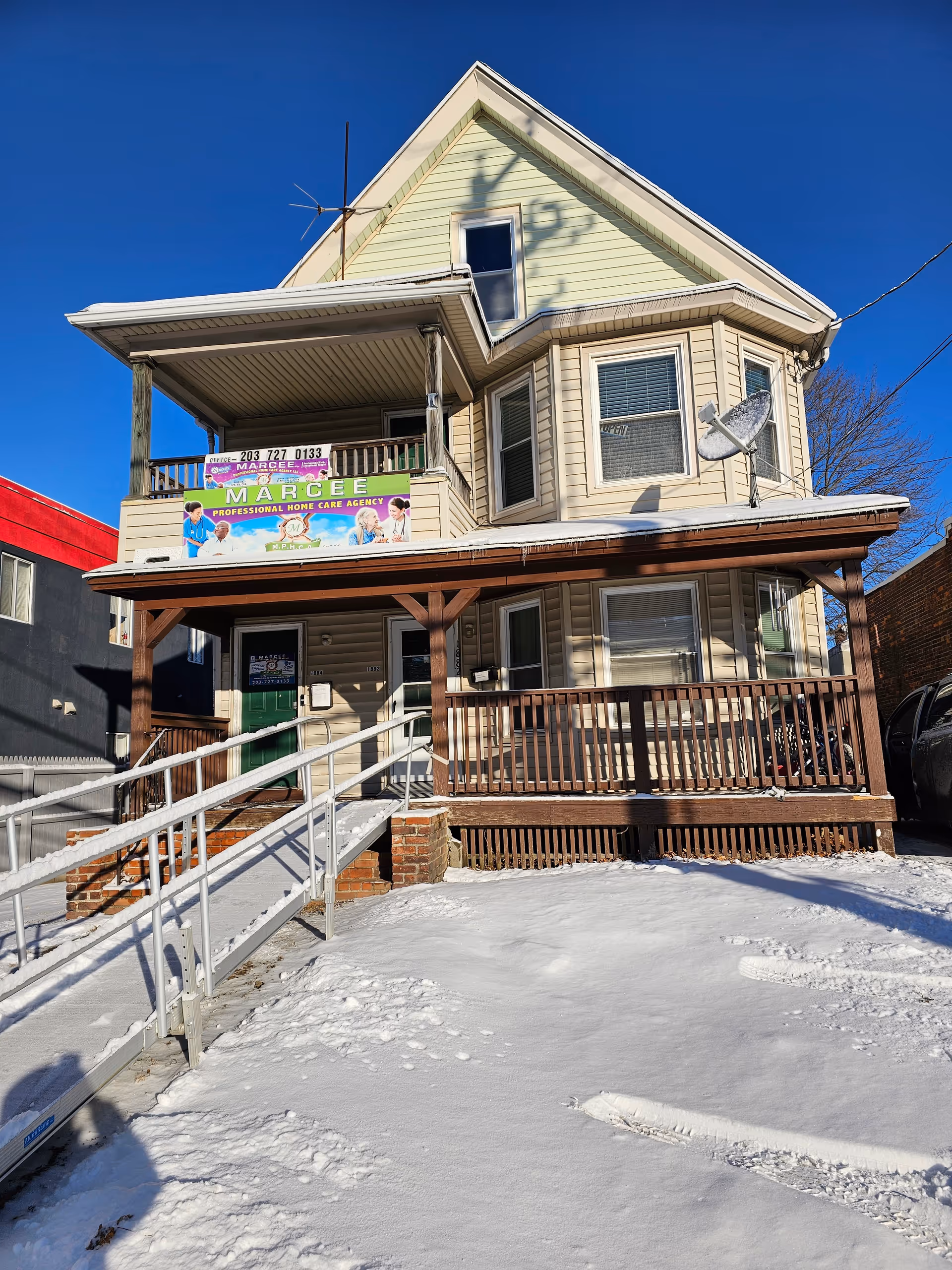 Two-story beige house with a wraparound porch and ramp, signage for Marcee Professional Home Care Agency.