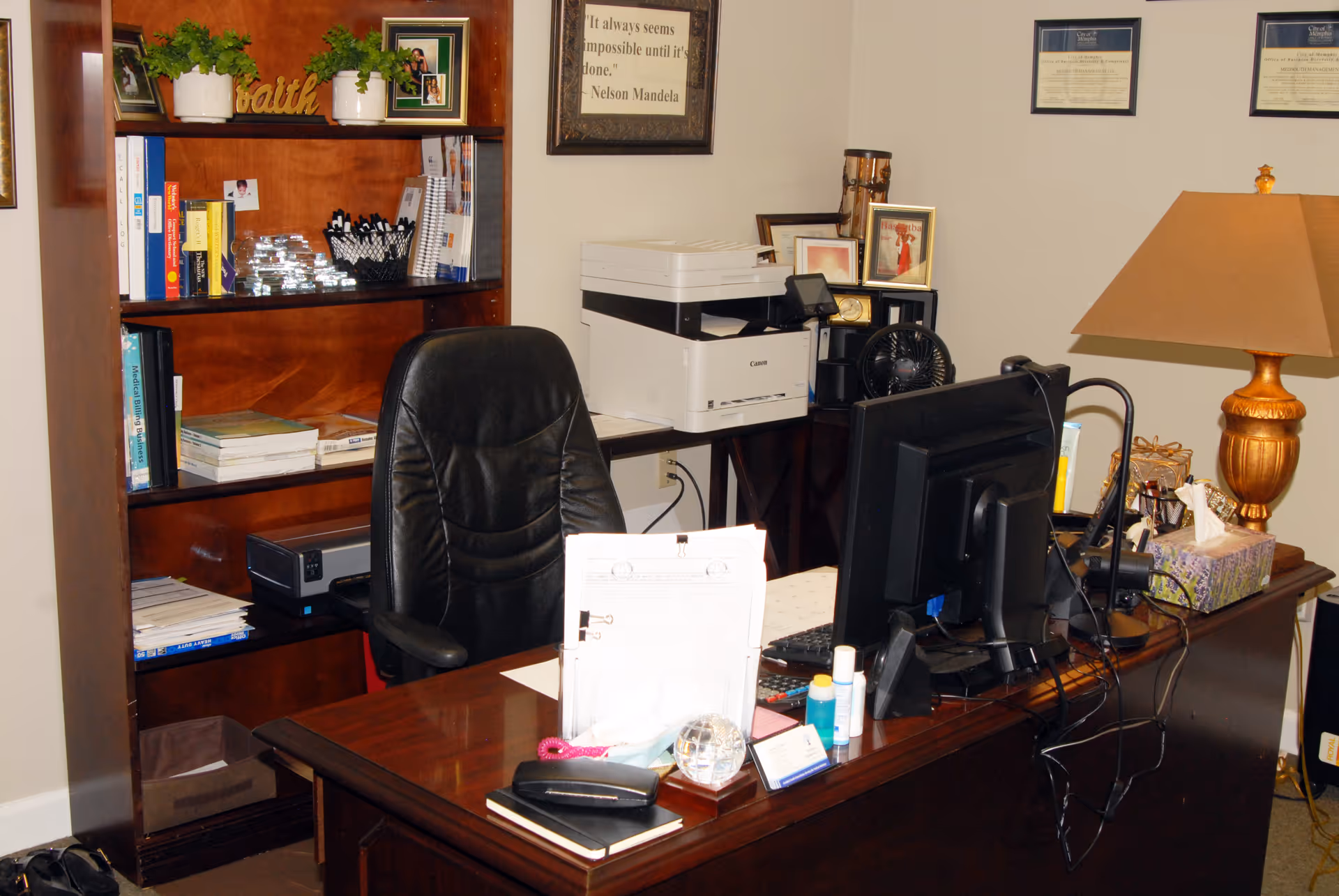 Office workspace with desk, computer, printer, and shelves in a senior facility admin area.