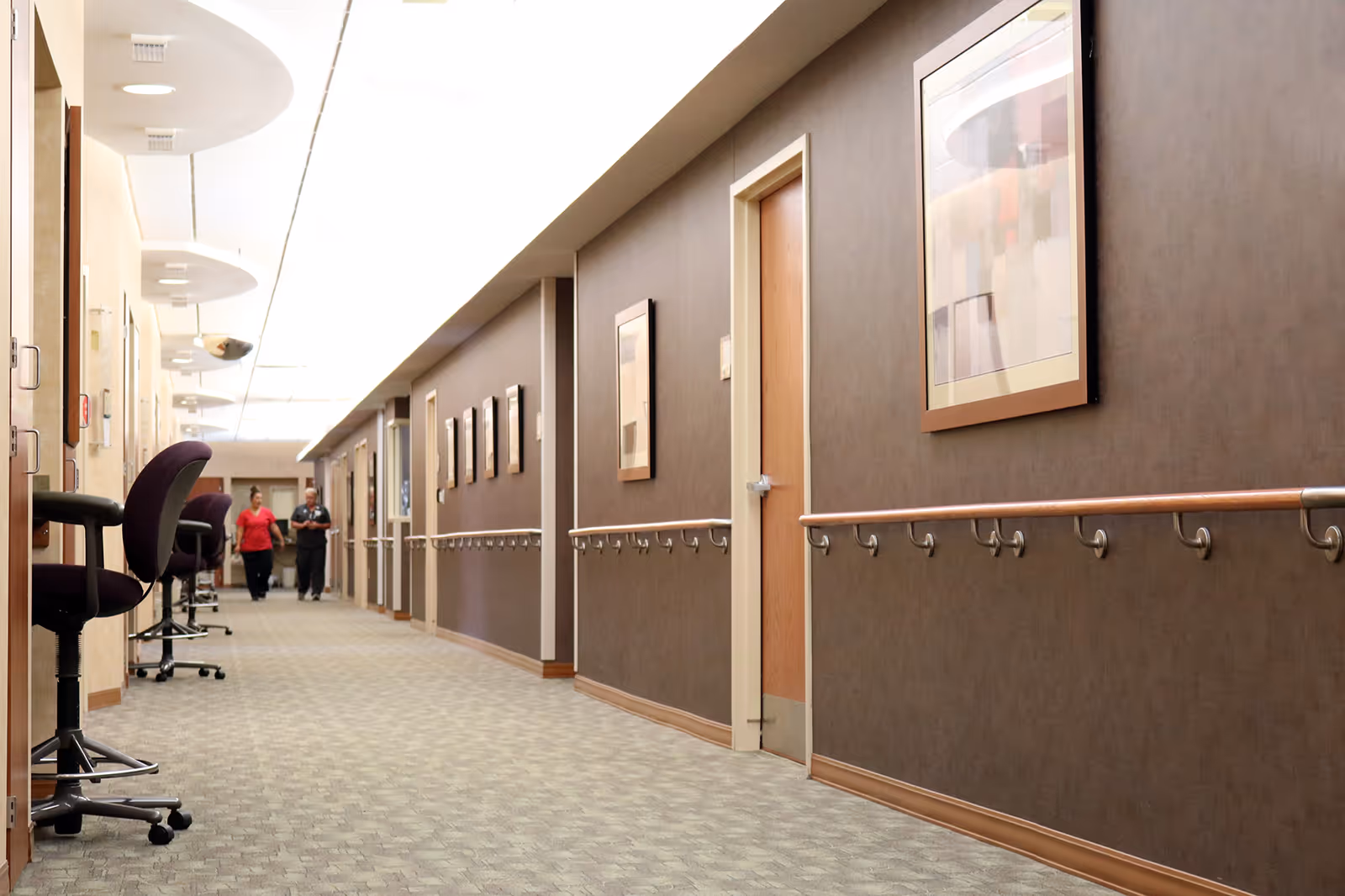 Long, well-lit hallway in Burgess Health Center with chairs, artwork, and handrails.