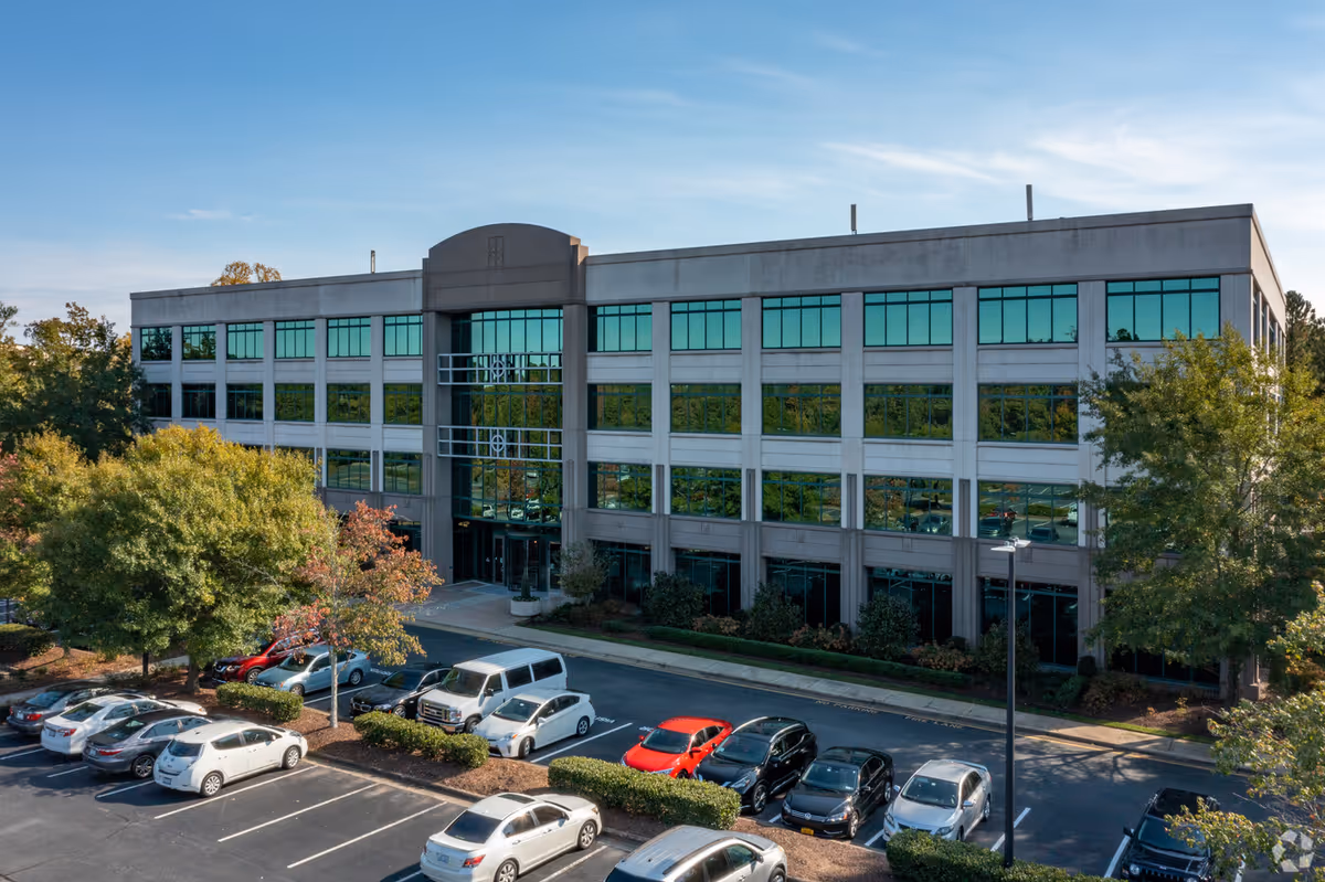 A modern, multi-story building with a glass entrance and surrounding parking.