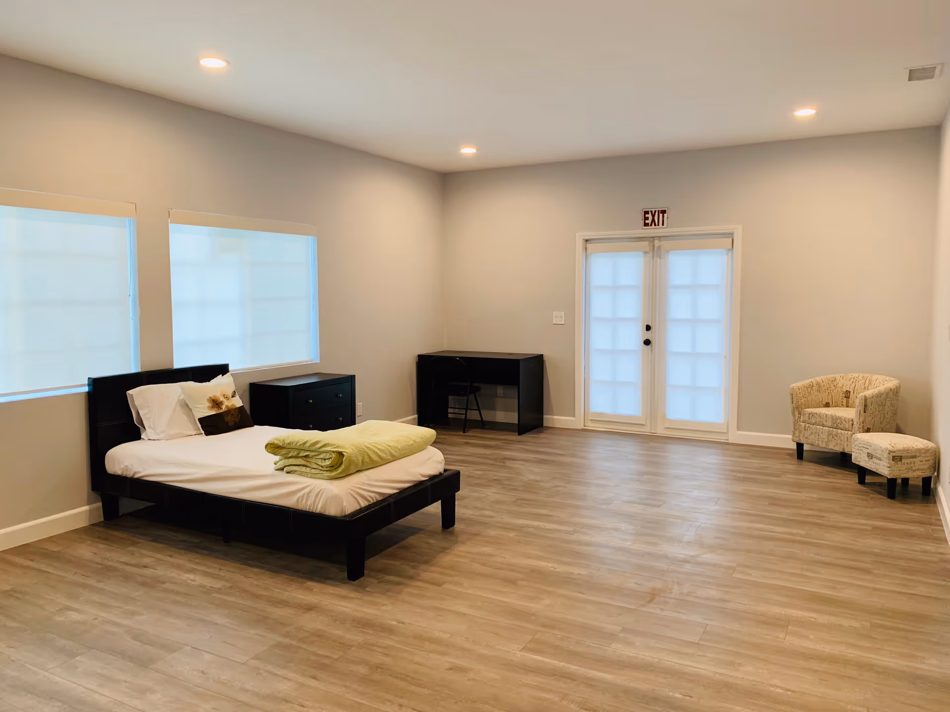 Spacious bedroom with a bed, dresser, desk, seating area, and frosted exit doors.