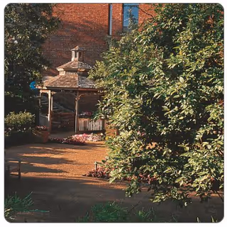 Outdoor courtyard featuring a gazebo, brick building backdrop, walking path, and surrounding trees.