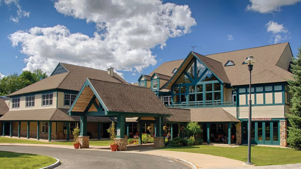 Multi-story lodge with a large covered entrance, tall triangular glass windows, and landscaped lawn under a blue sky.