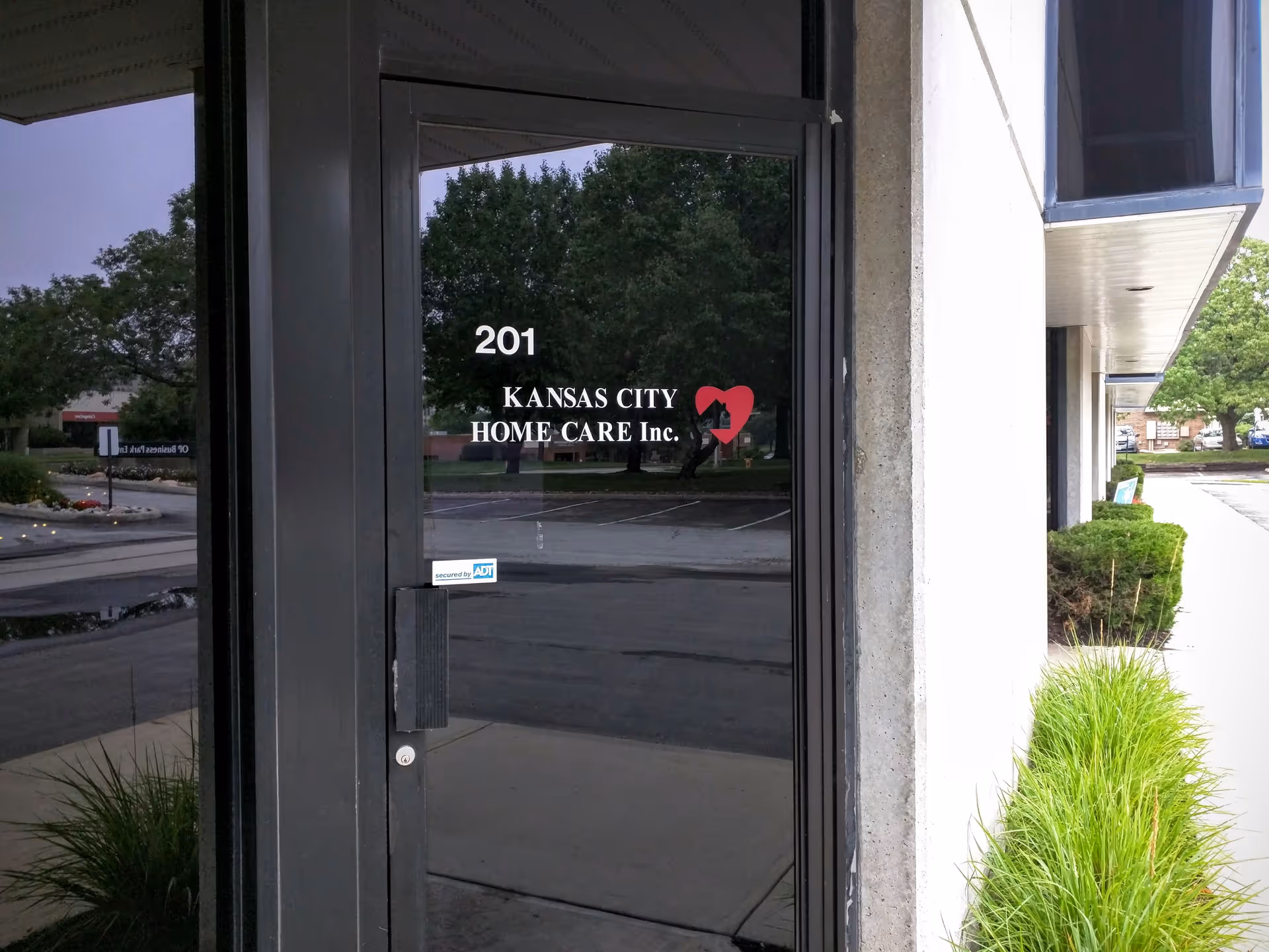 Glass entrance door with signage reading Kansas City Home Care Inc. in front of building.