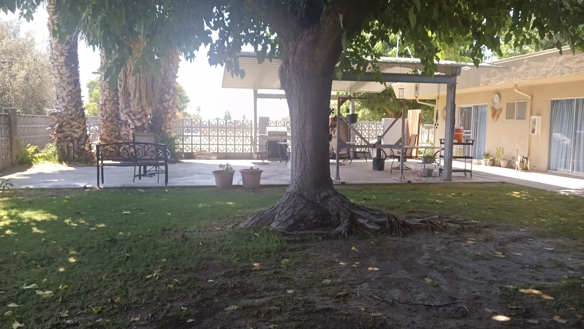 Outdoor patio at Delano PostAcute Care with benches, trees, and shaded seating.