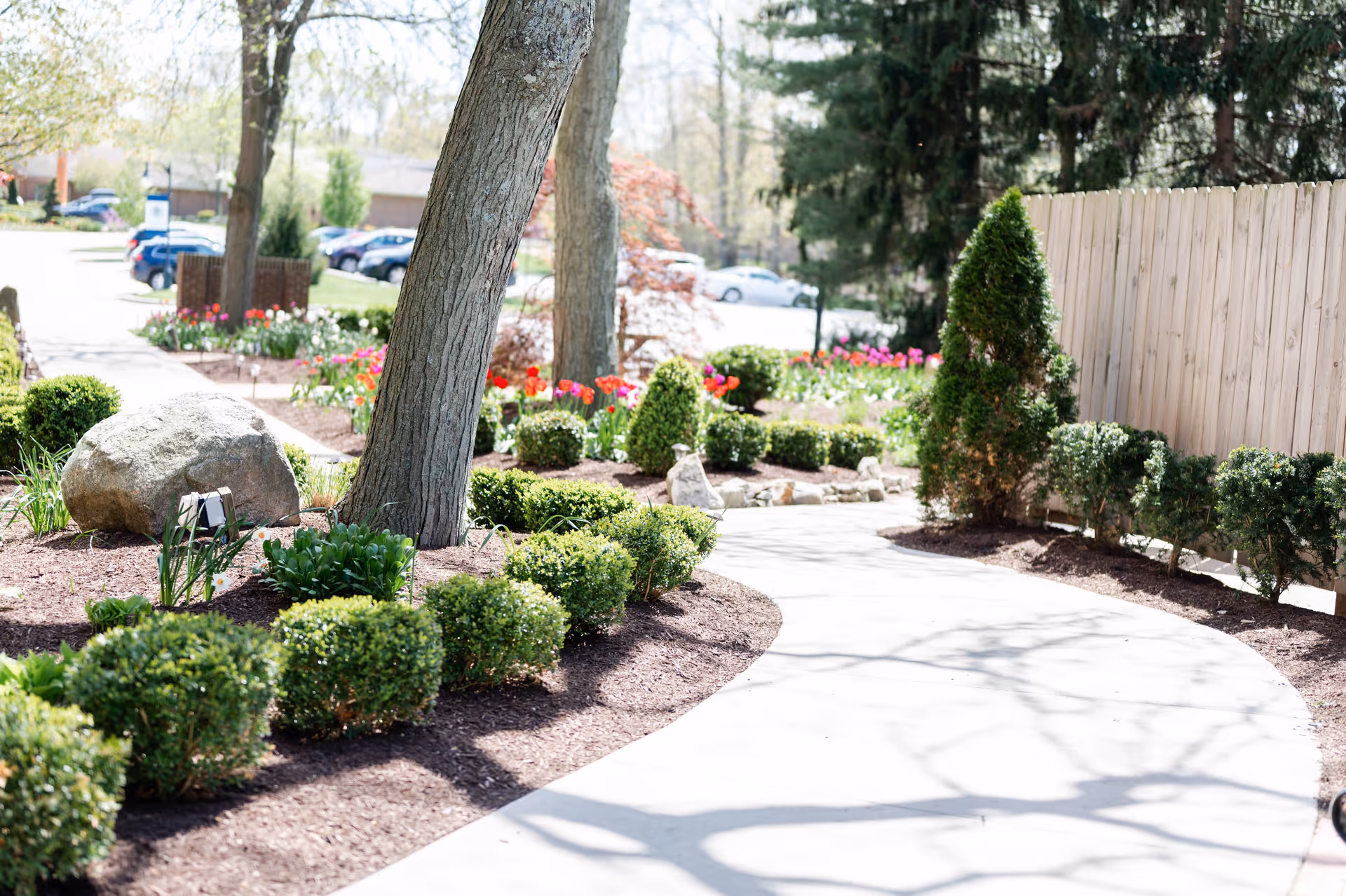 Curved concrete walkway winds through landscaped shrubs and trees.
