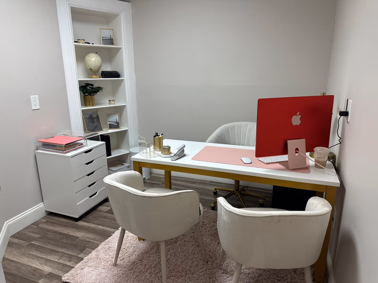Office desk with pink equipment, white chairs, and shelving in a small room.