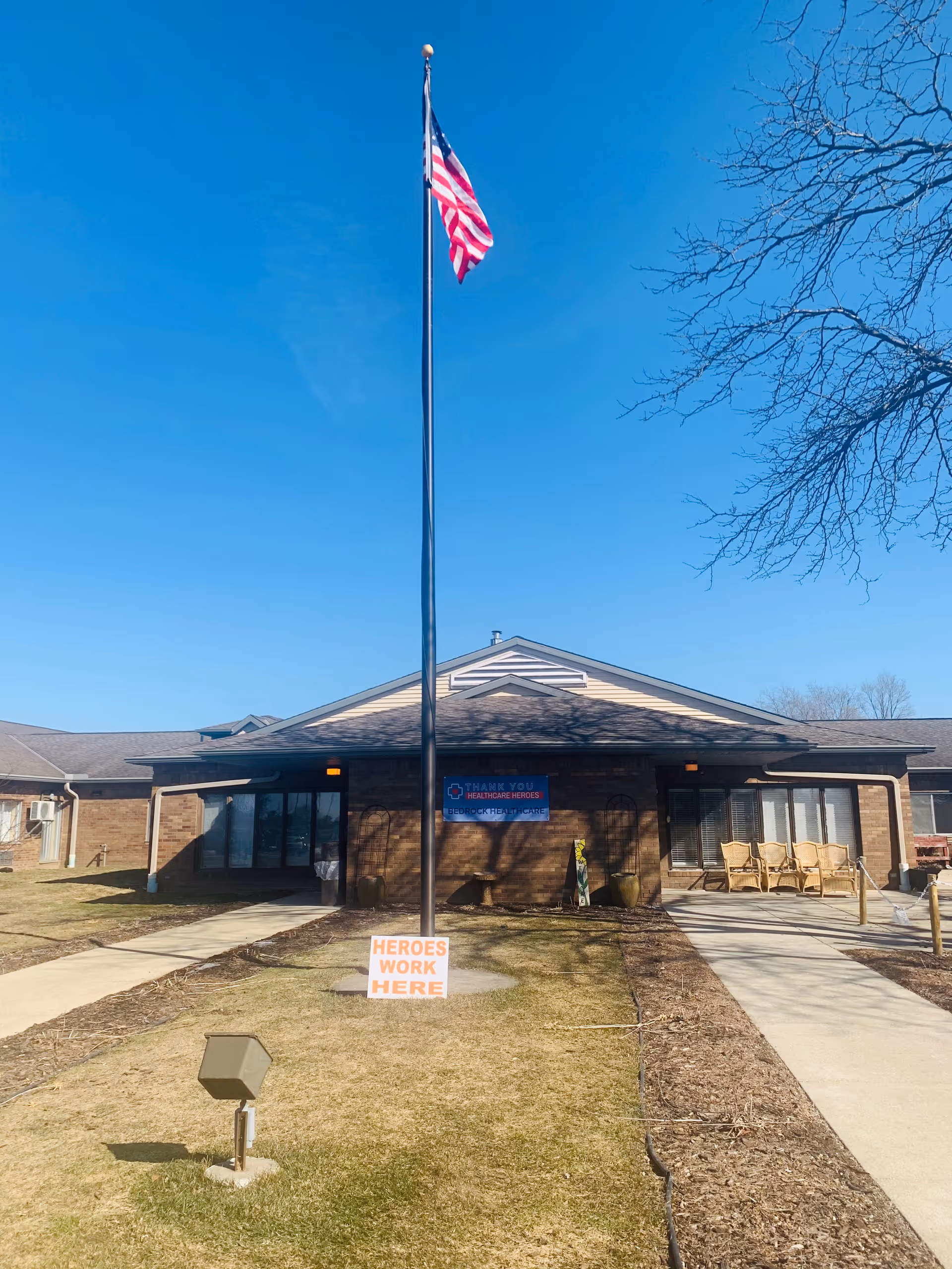Brick senior living facility exterior with flagpole, American flag, and outdoor seating.