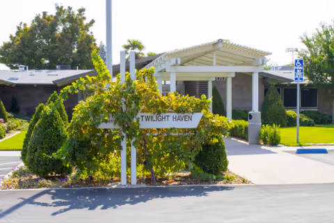 Front entrance of a single-story senior living building with a covered walkway, manicured landscaping, and a sign reading "Twilight Haven".