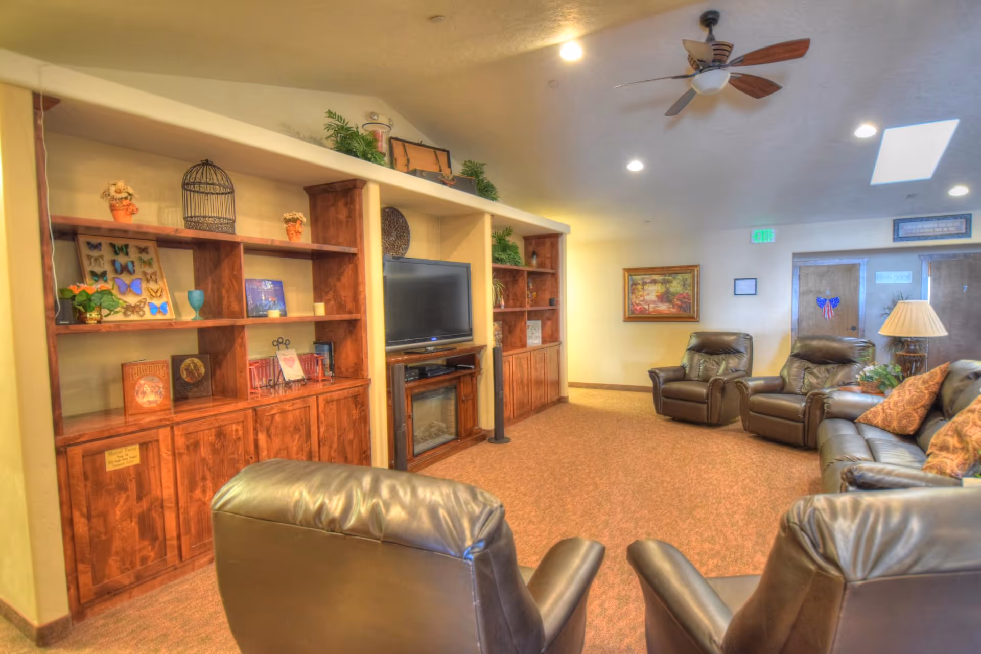 Cozy living room in a senior facility with leather recliners, a TV, and wood shelves.
