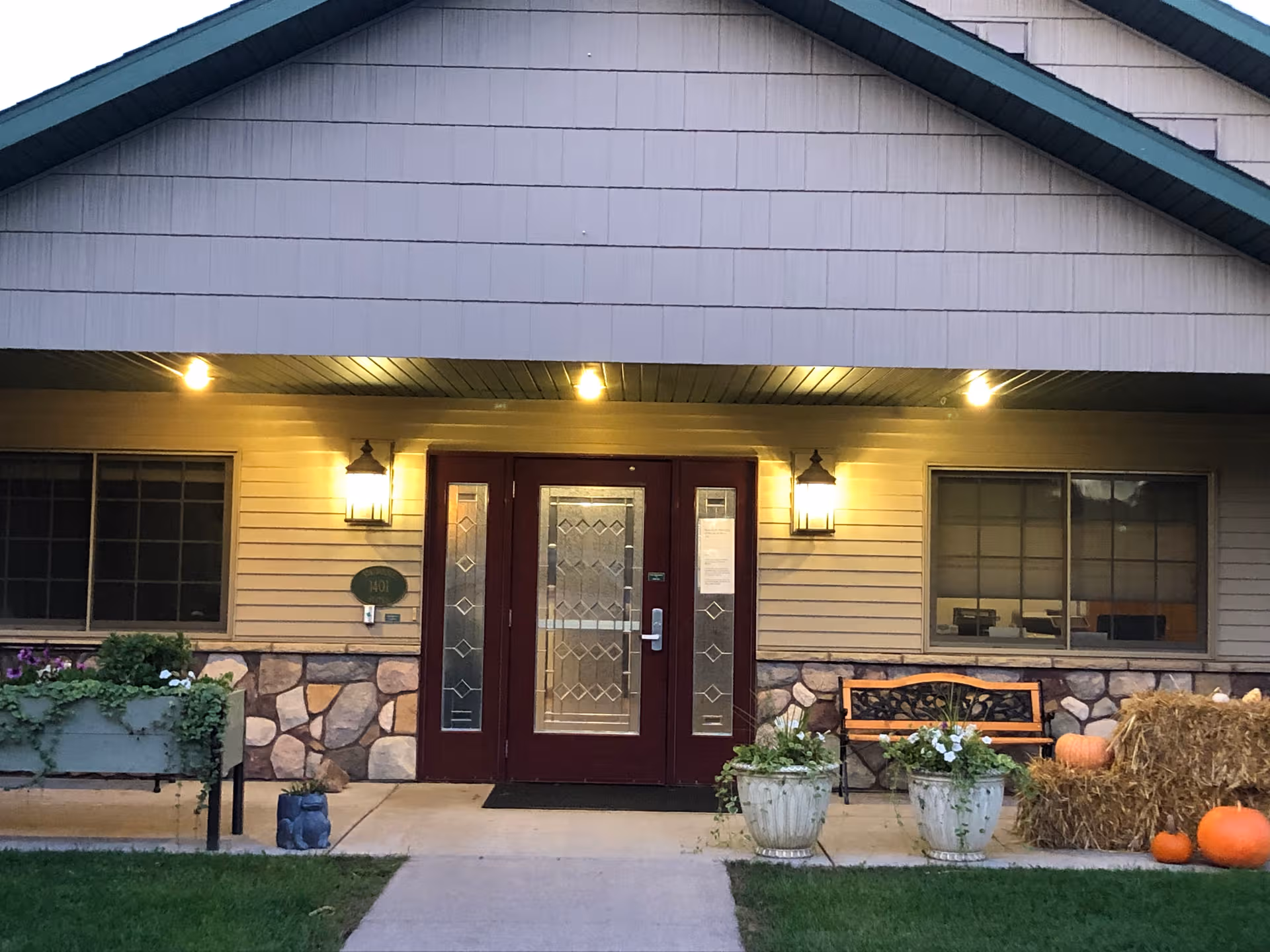 Front entrance of a senior living facility with double glass doors, lights, and planters.