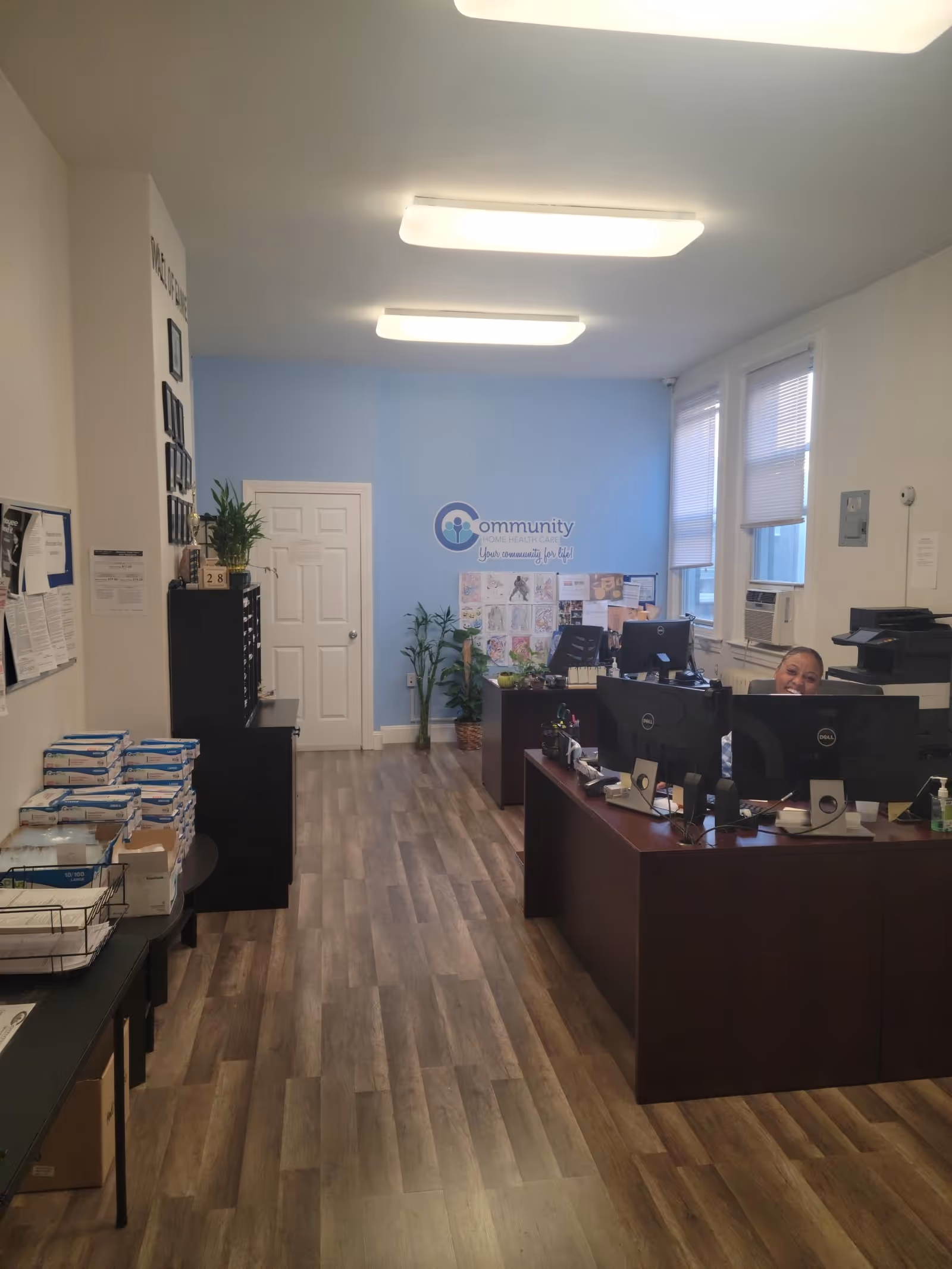 Reception area of Community Homecare recruiting office with desks, computers, plants, and a logo.