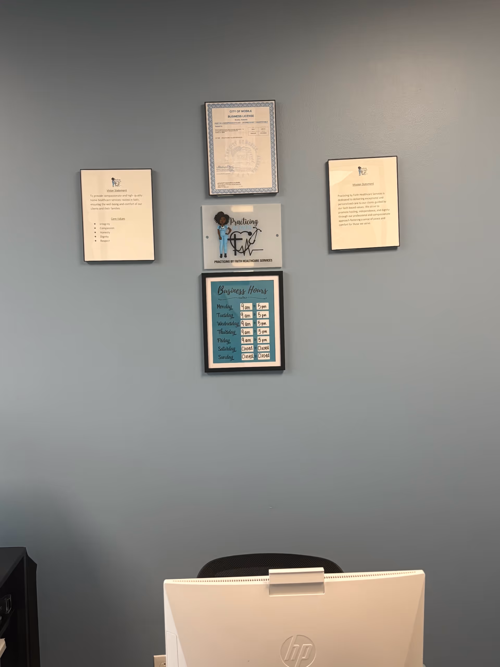 Office wall with framed documents and a computer monitor on a desk against a blue wall