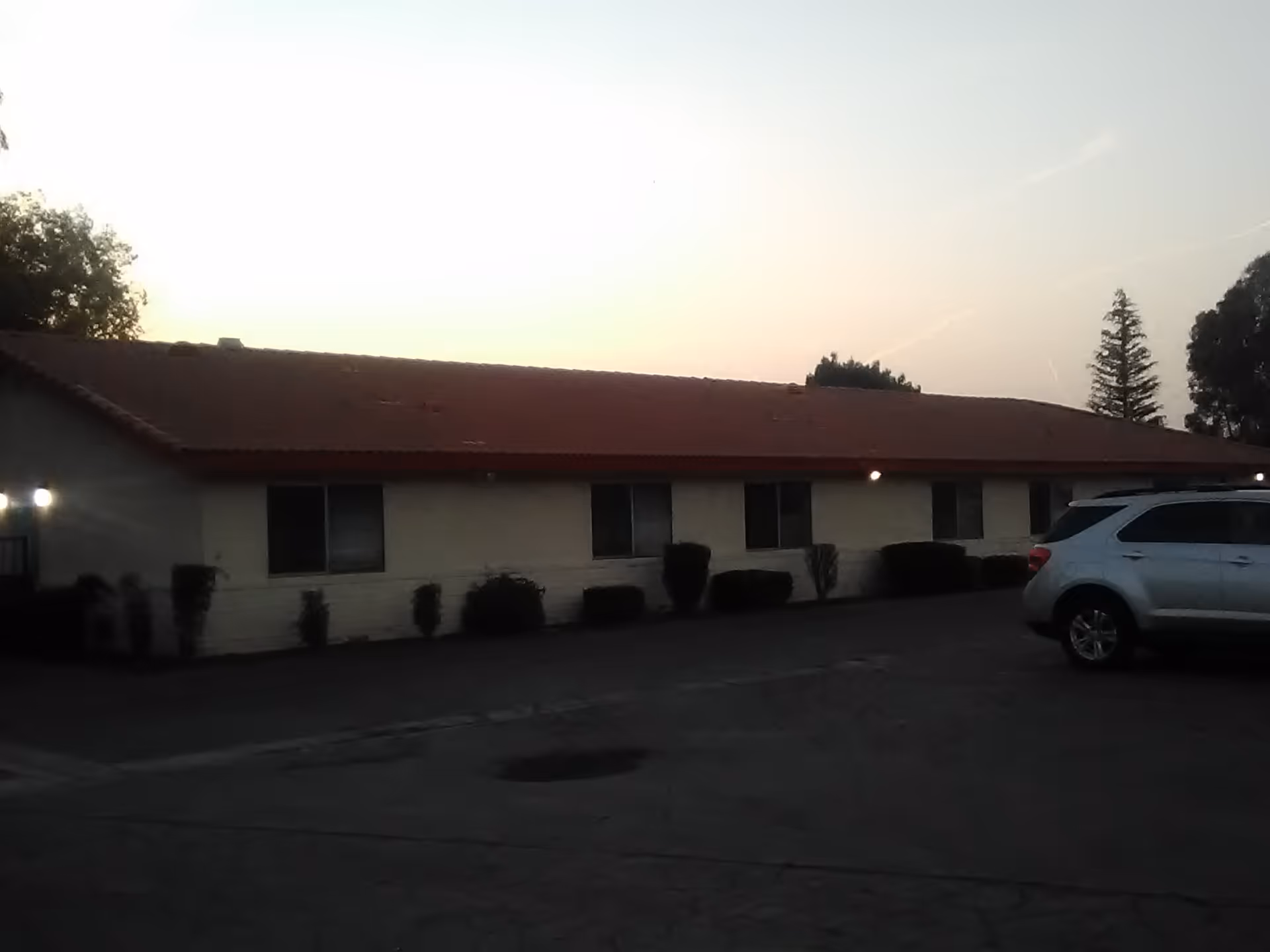 Exterior view of a single-story facility with red roof and parked SUV.