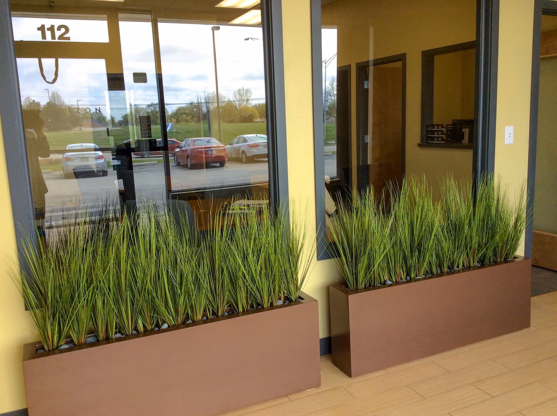 Indoor reception area with two brown planter boxes filled with tall green grasses by glass doors