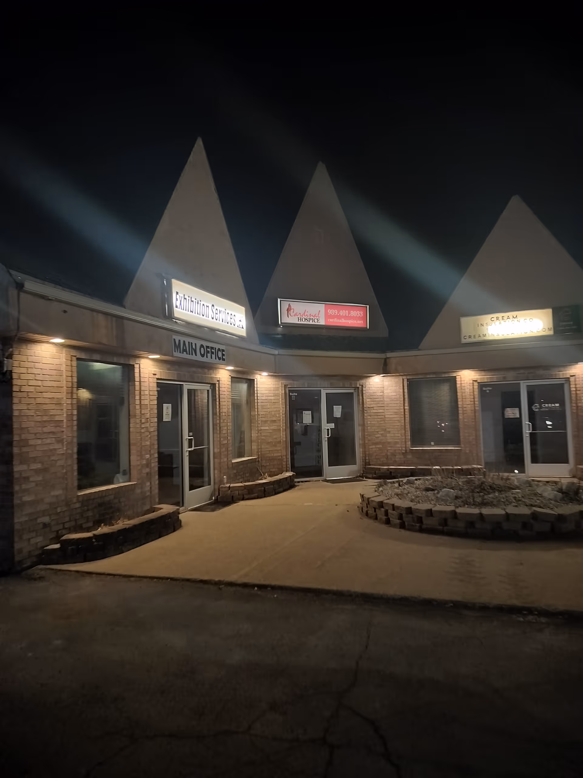 Night exterior of a brick building with office doors and illuminated signs.