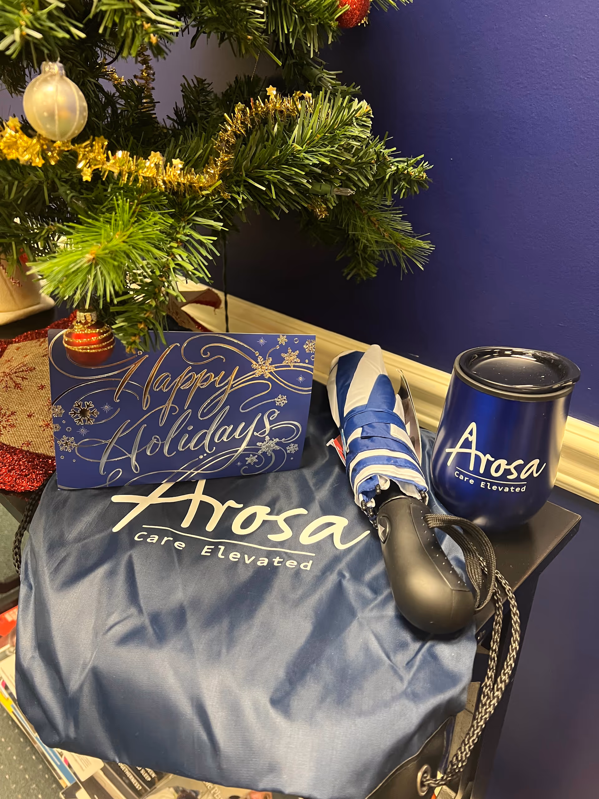 Close-up of an indoor holiday display with a blue Arosa bag, mug, and card.
