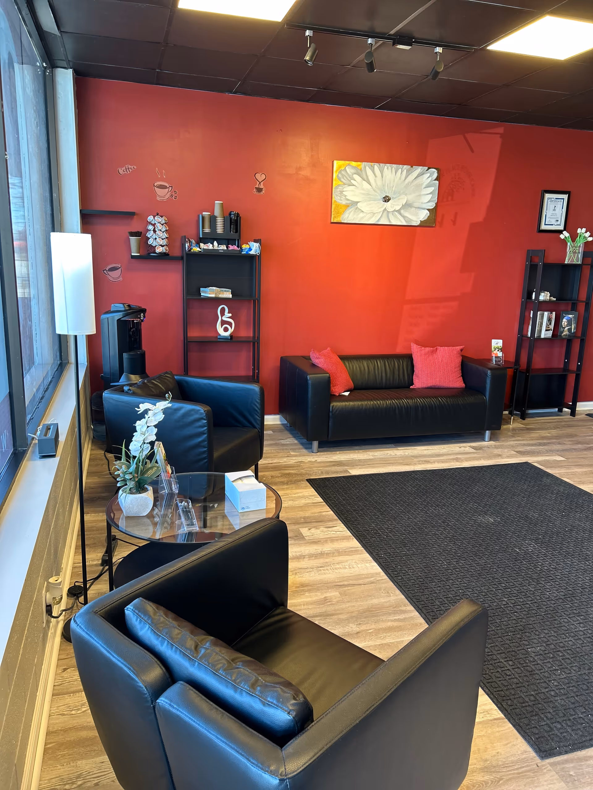 A lounge area with black leather couches, red wall, and shelves in a modern reception.