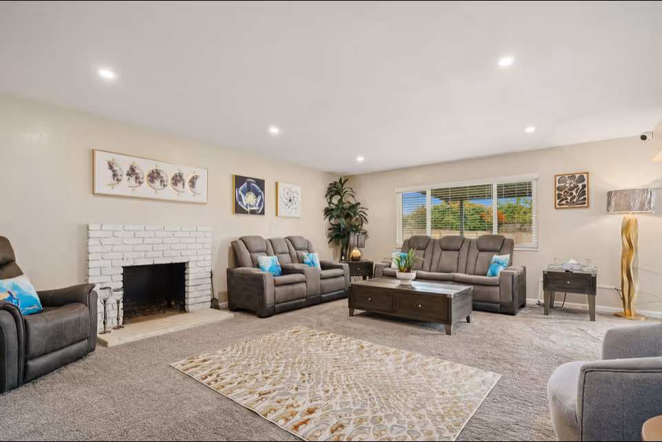 Bright common living room with gray reclining sofas, wood coffee table, and fireplace.