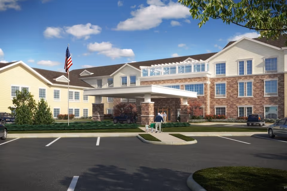 Exterior view of Alto Overland Park senior living facility showing a large building with a covered entrance, an American flag on a flagpole, several parked cars, and a person walking a dog on the sidewalk leading to the entrance under a partly cloudy blue sky.