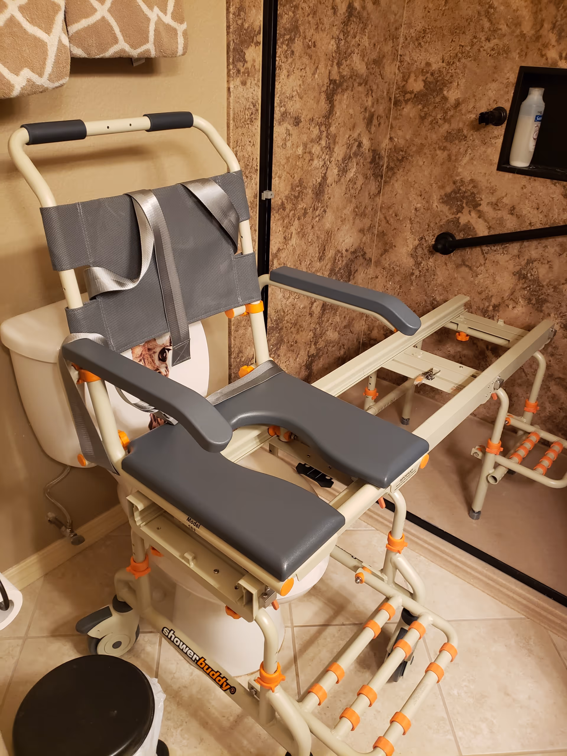 Adaptive shower chair with armrests and orange adjustable supports in a tiled bathroom.