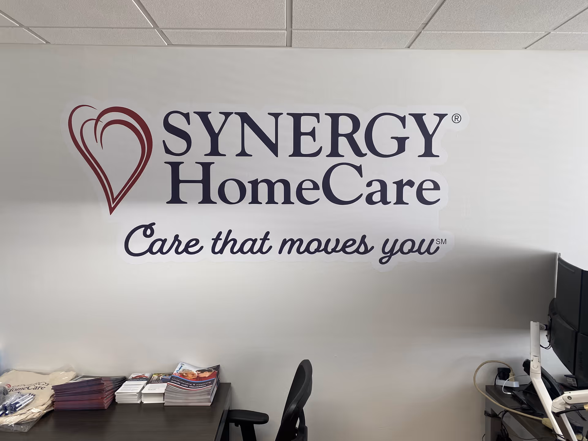 Indoor reception area with SYNERGY HomeCare logo on wall and desk with brochures.