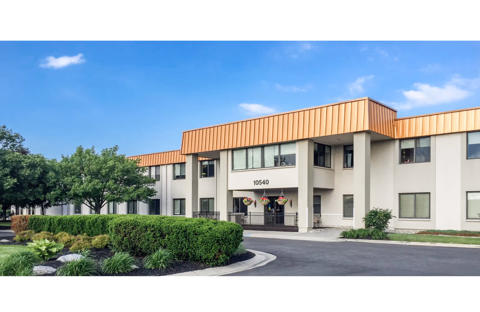 Exterior view of Legacy Perrysburg senior living facility with landscaping and a clear sky.