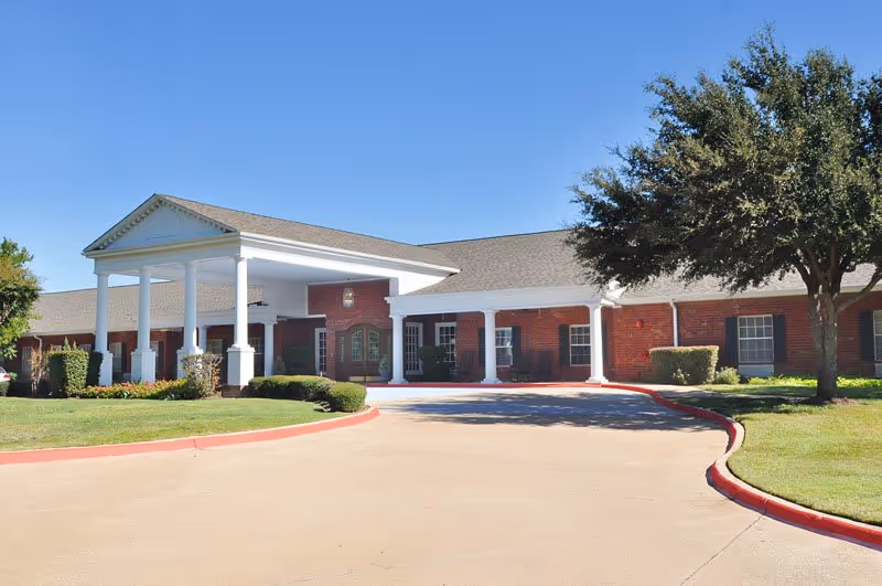 Brick senior living facility with white columns and landscaped entrance, curved driveway in front.