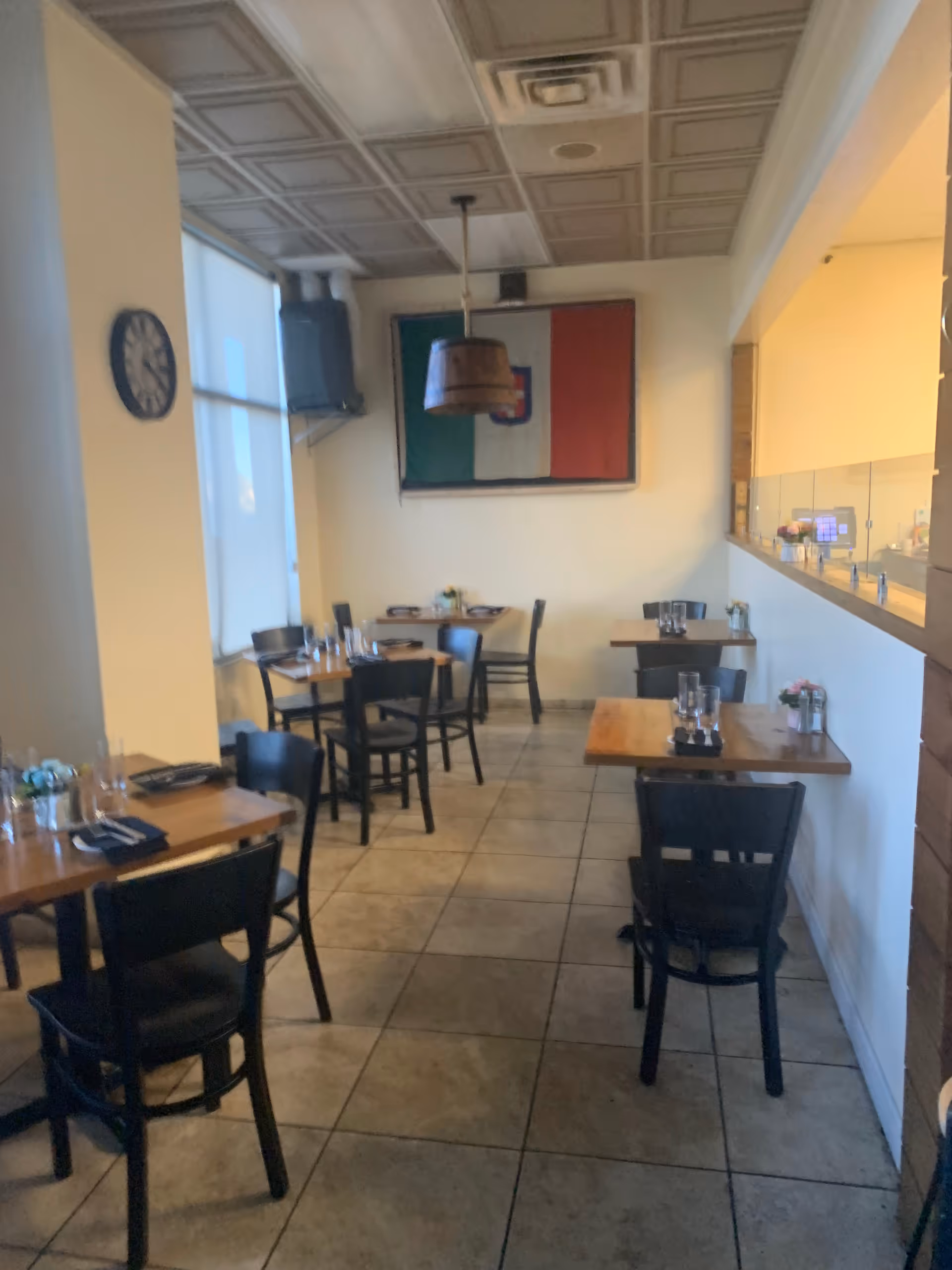 Dining room in a senior facility with wooden tables, black chairs, and Italian flag wall art.