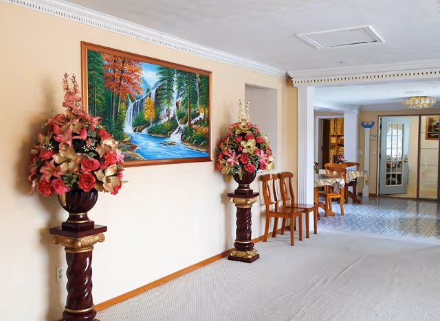 Hallway interior of Pasadena Home Care II with floral arrangements, a painting, and seating.