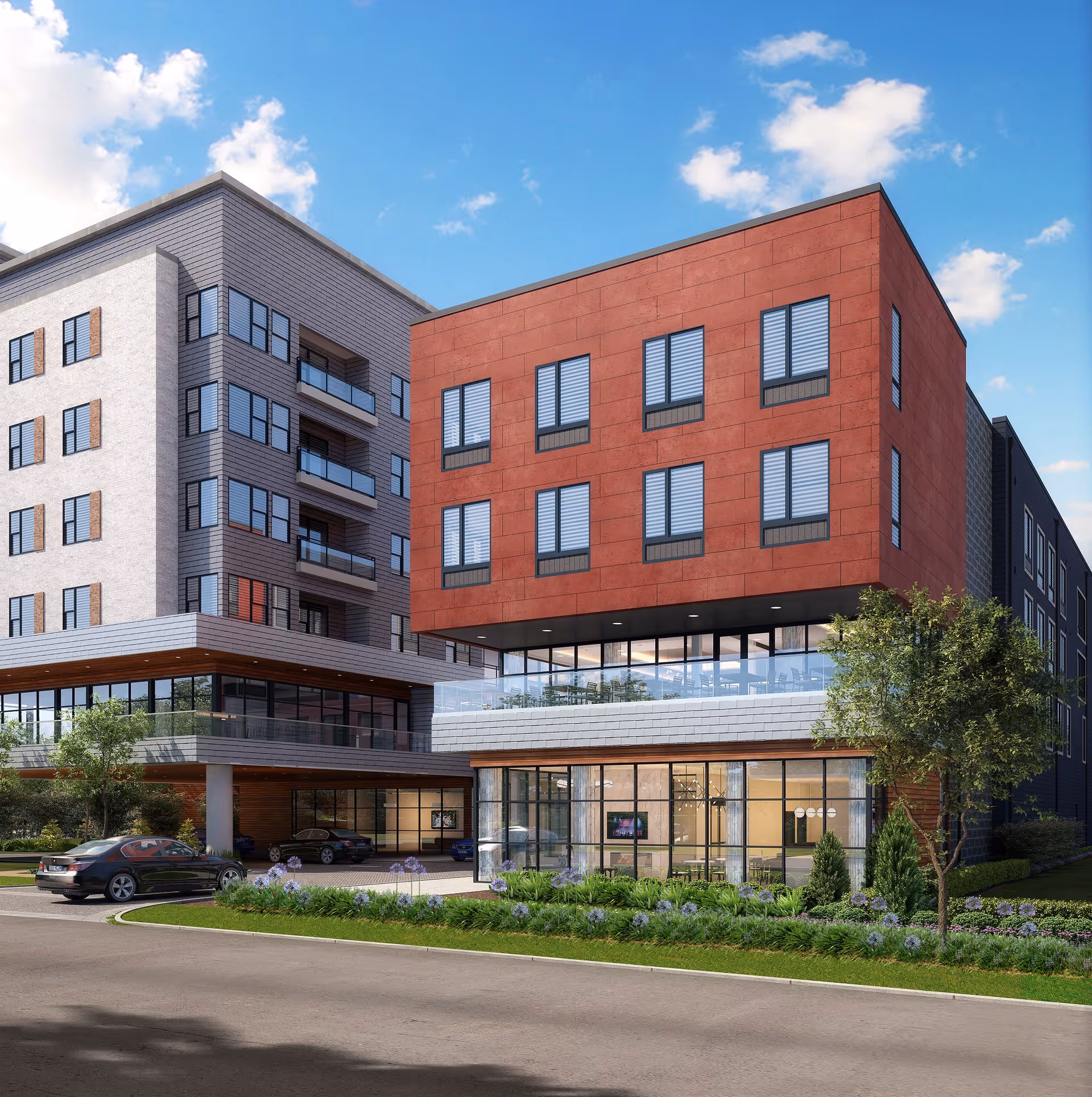 Exterior view of a modern multi-story senior living facility with a combination of red and gray facade, large windows, balconies, landscaped greenery, and parked cars in front under a blue sky with scattered clouds.