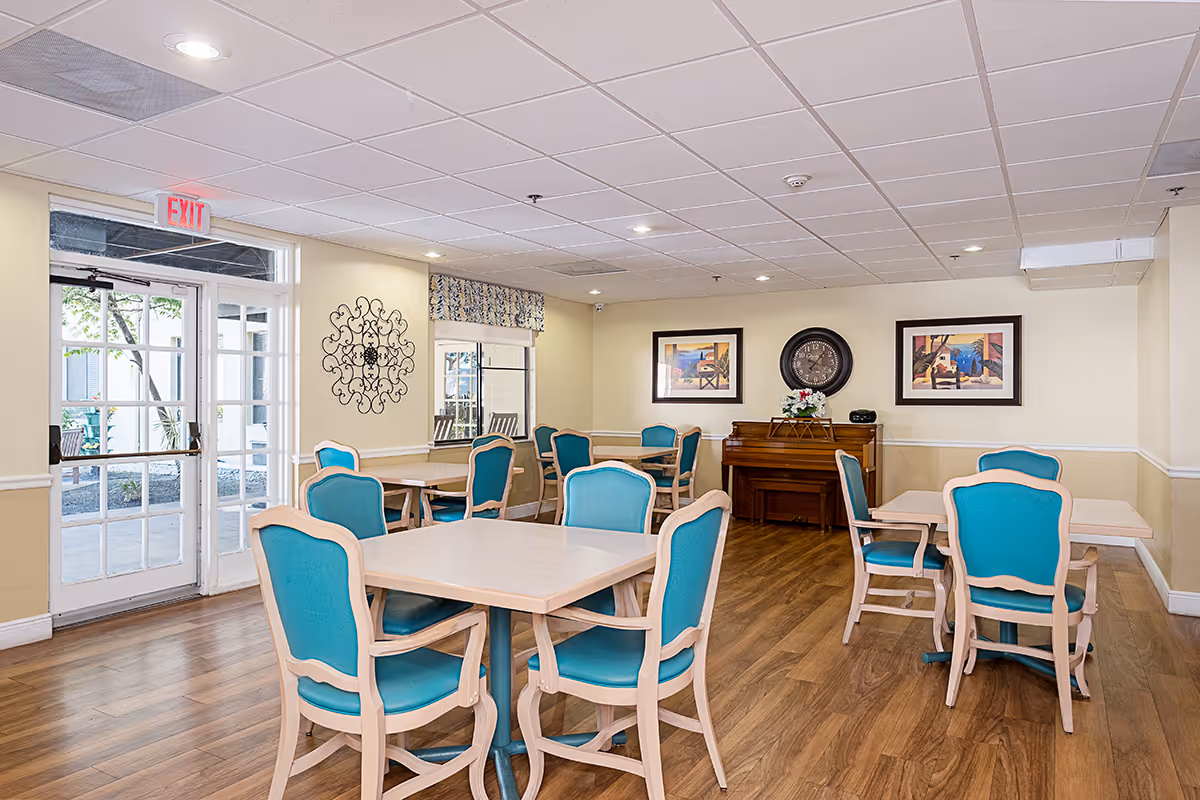 Bright senior living dining area with turquoise chairs around light wood tables.