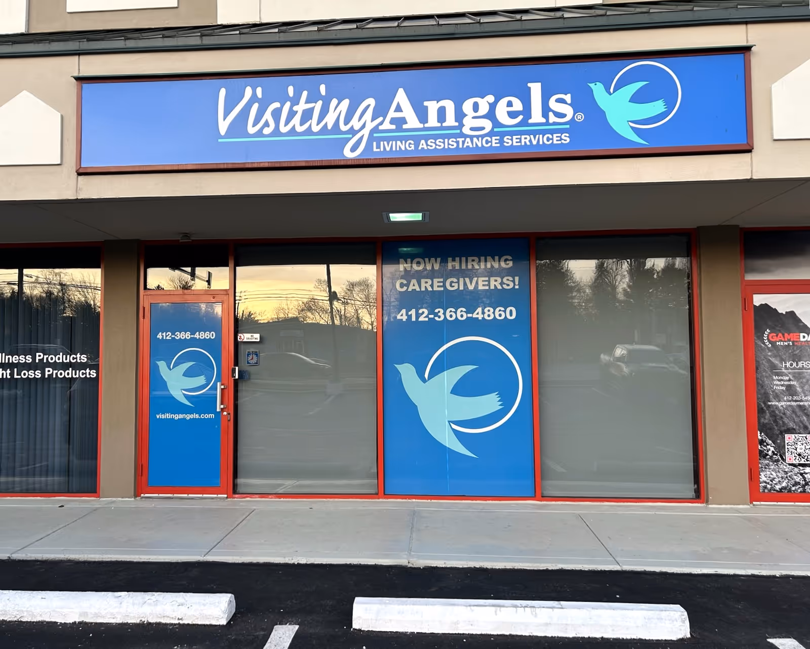 Storefront of Visiting Angels Senior Home Care with blue sign and large window ads.