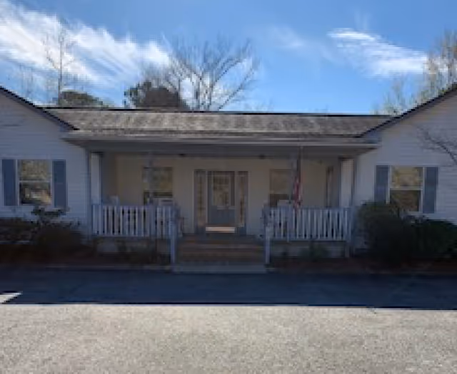 White single-story senior home with covered front porch, steps, and blue shutters