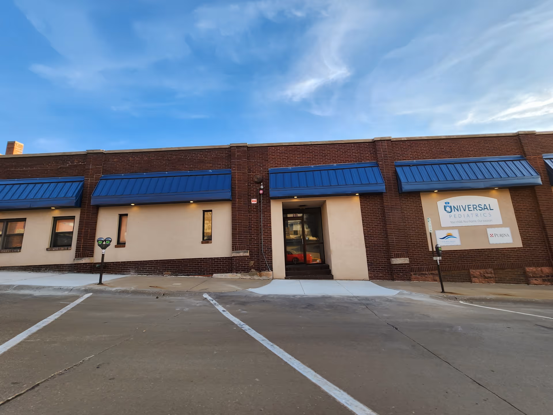 Exterior view of a brick facility with blue awnings and a sign.
