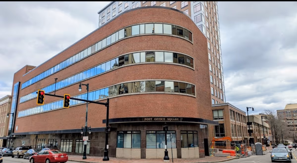 Curved brick office building on a street corner with traffic lights and parked cars