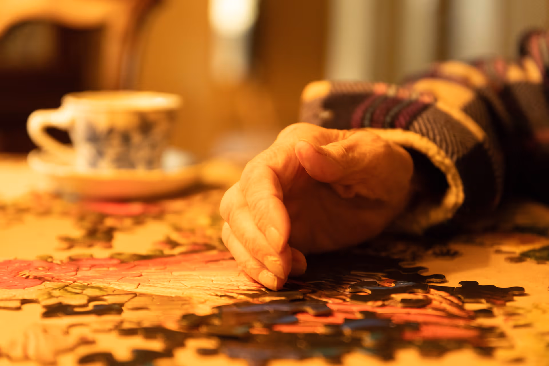 Close-up of an elderly hand resting on a jigsaw puzzle on a table.