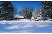 Snowy yard in front of a single-story facility surrounded by trees.