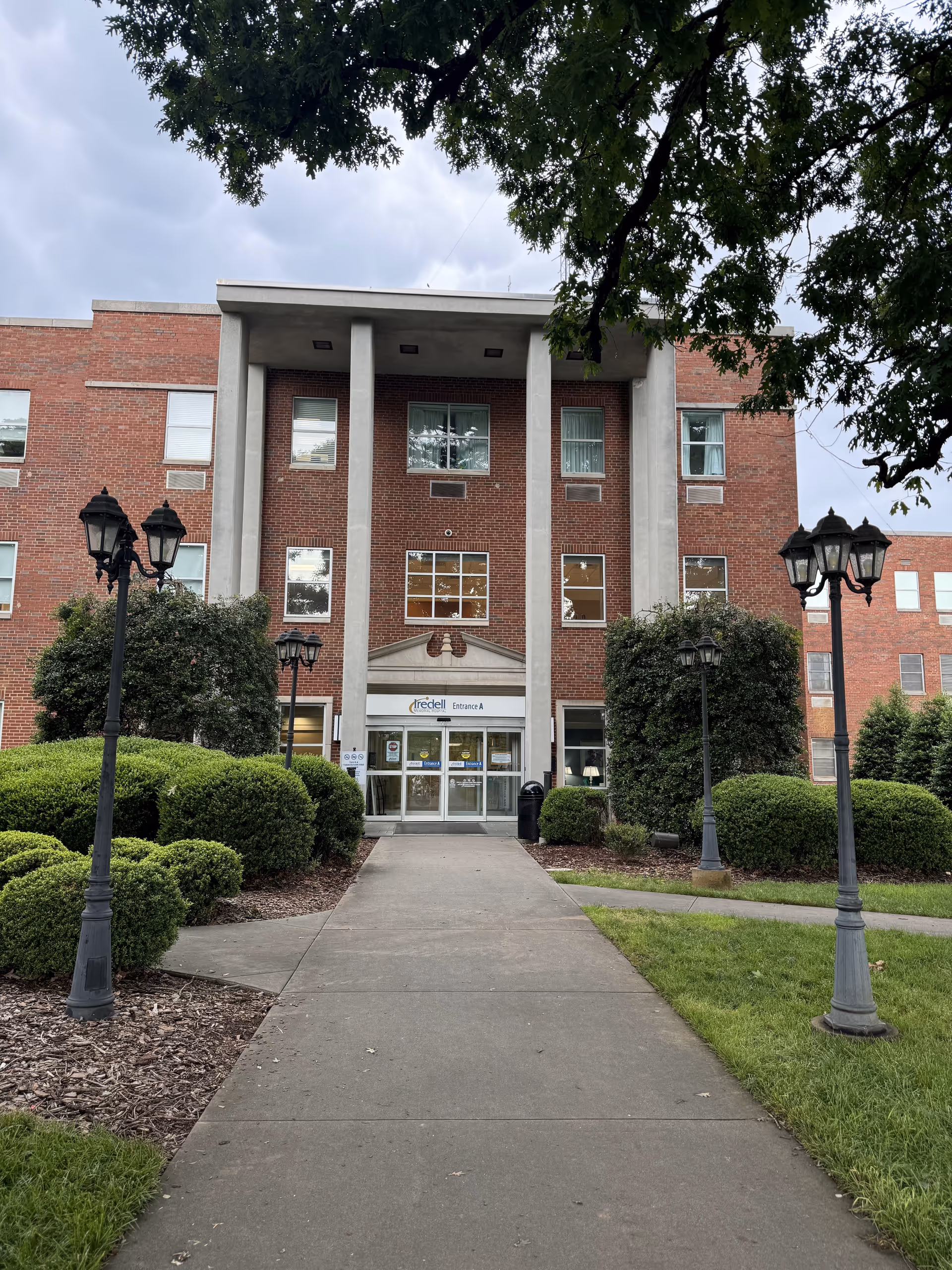 Brick senior living facility entrance with glass doors and lampposts along a walkway.