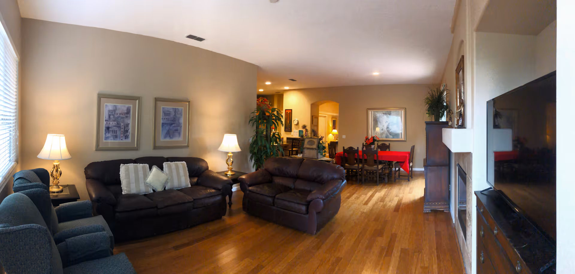 Spacious living room with leather sofas, lamps, framed art, and a dining area in back