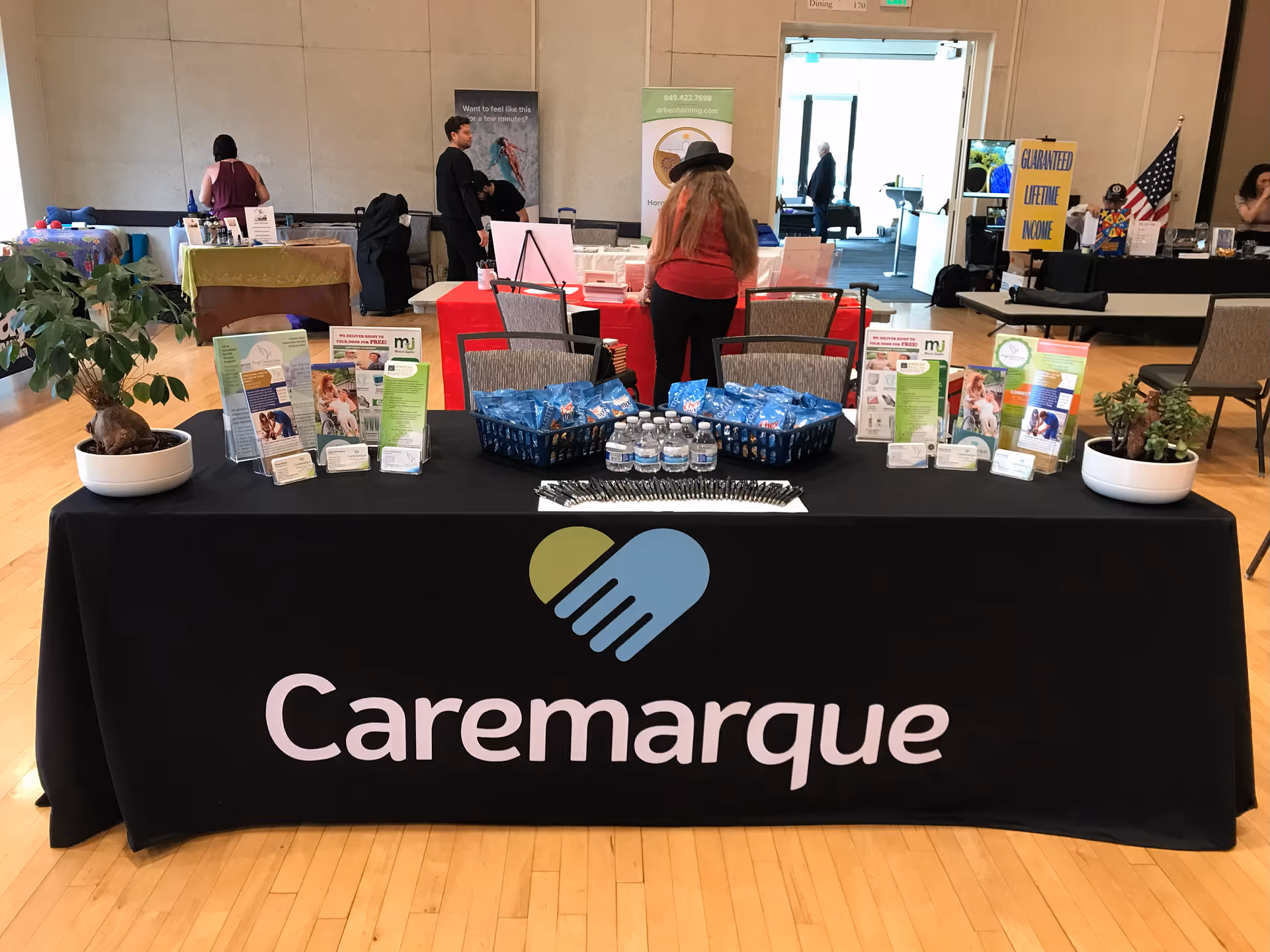 Indoor event booth with Caremarque branding, brochures, and bottled water on a long table.