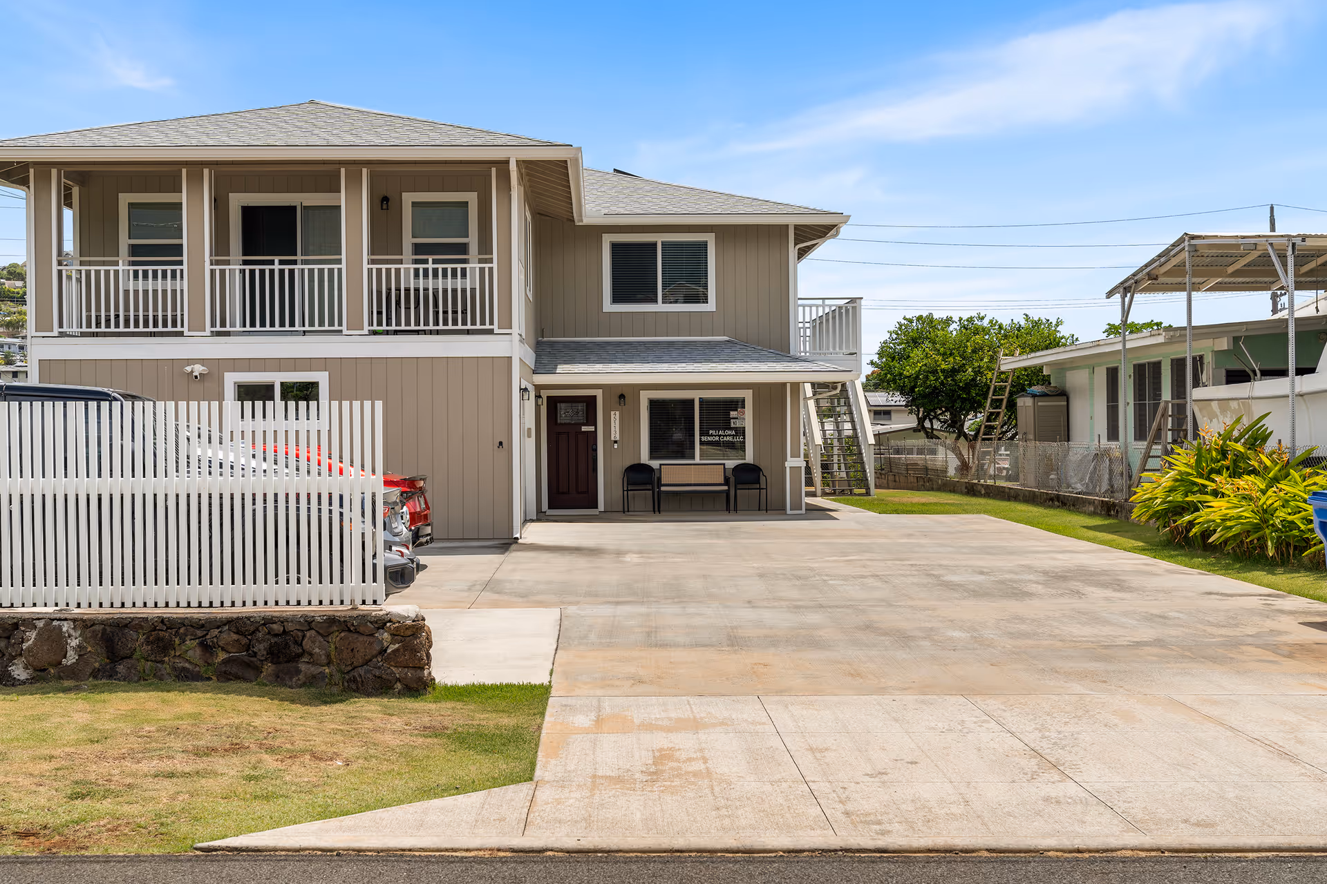 Two-story senior care building with driveway, parked car, front entrance, balcony, and surrounding yard.