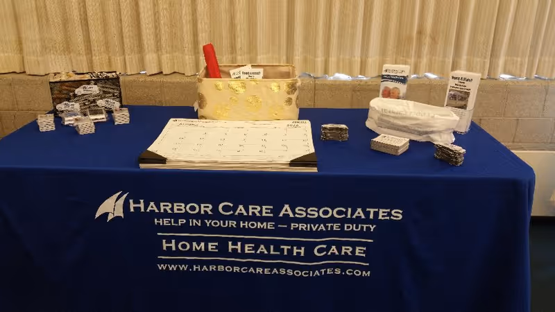 Blue table with Harbor Care Associates branding displays brochures and a calendar in an indoor setting.