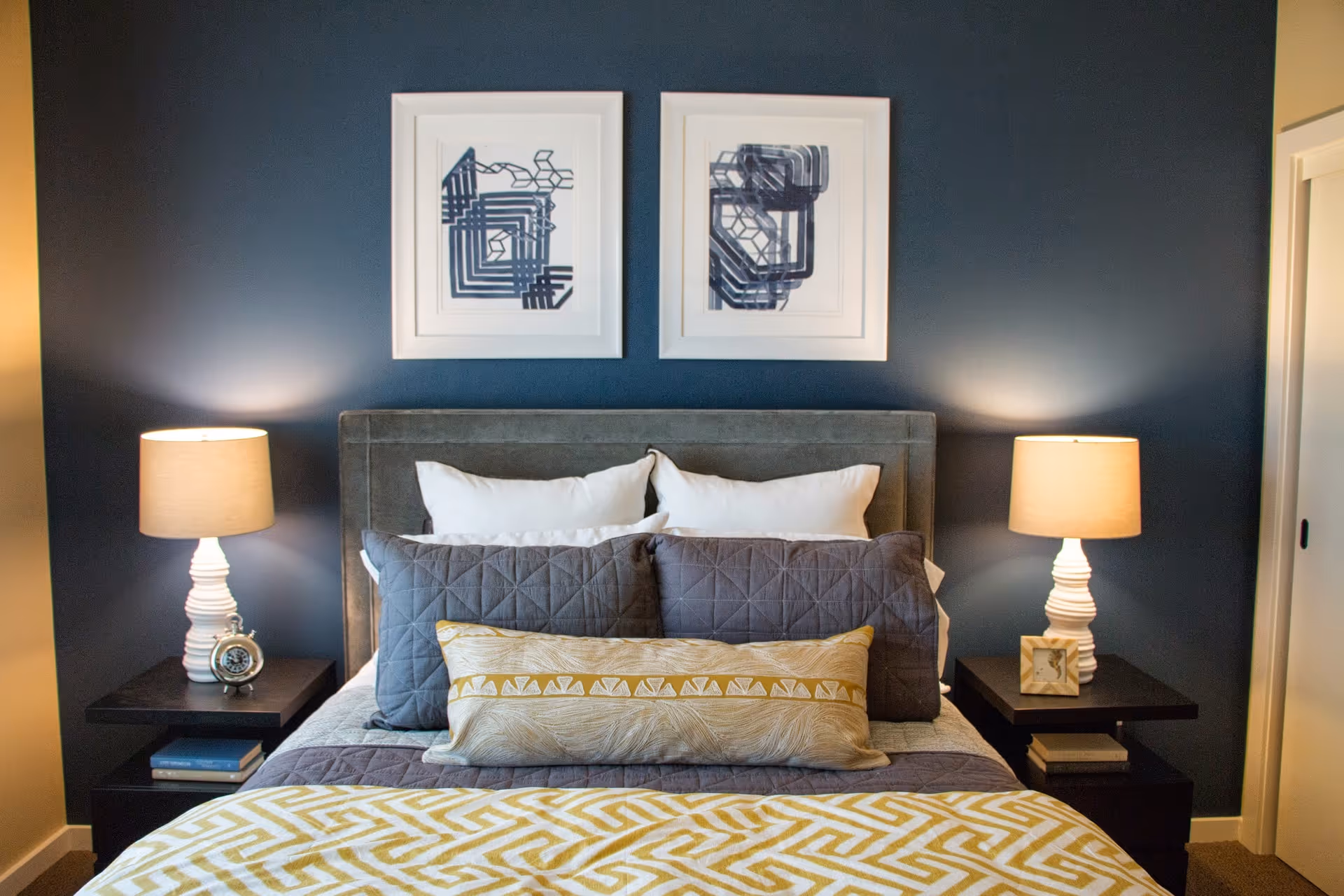 Bedroom with dark blue accent wall, framed abstract art, bed, nightstands, and lamps.