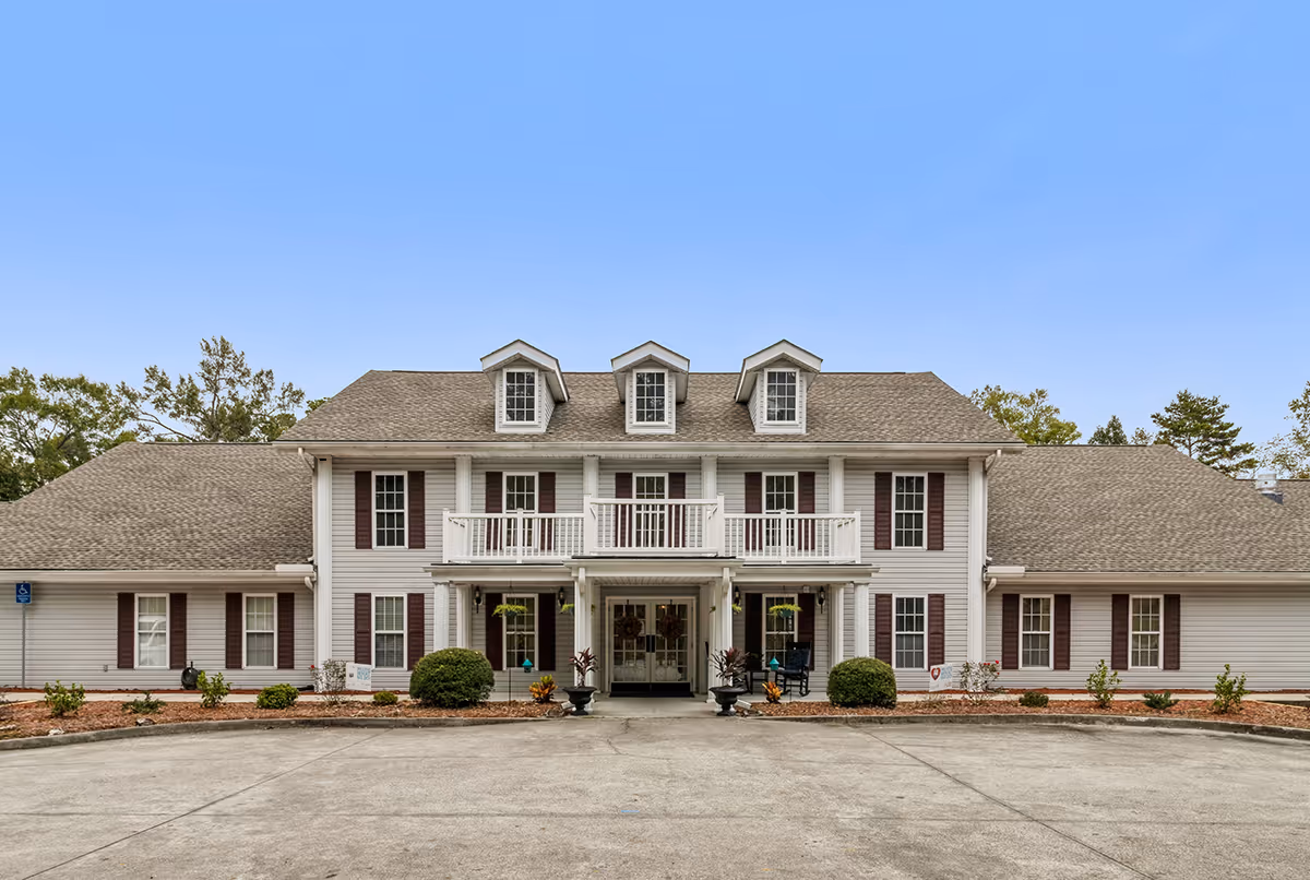 Two-story white senior living facility with a centered entrance, balconies, and dormer windows.
