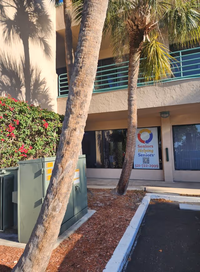 Exterior view of Seniors Helping Seniors Brevard County facility with palm trees and banner.